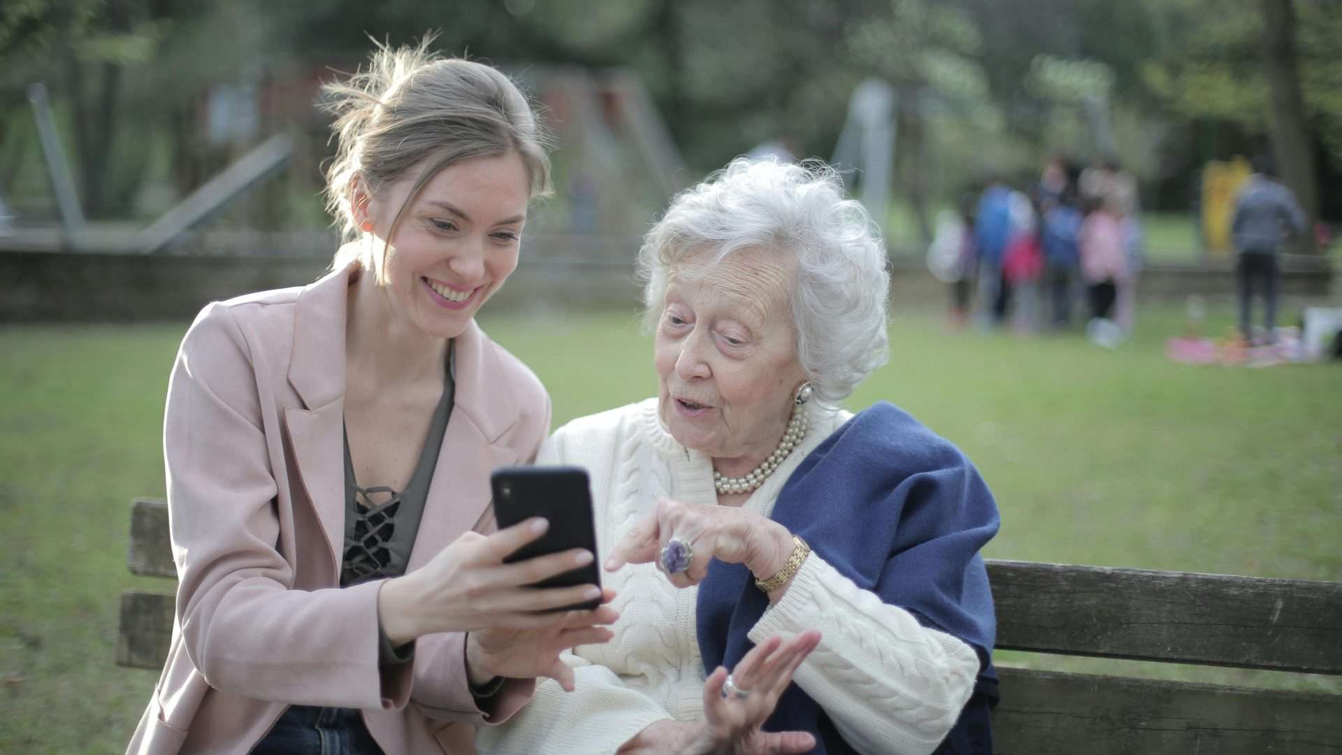Golpes contra idosos, foto ilustrativa de mulher mais jovem mostrando celular para idosa