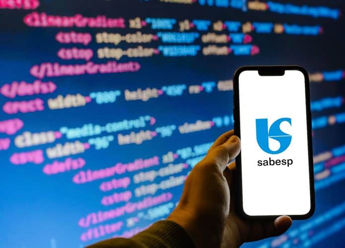Logo da Sabesp em um smartphone; no fundo códigos de computador