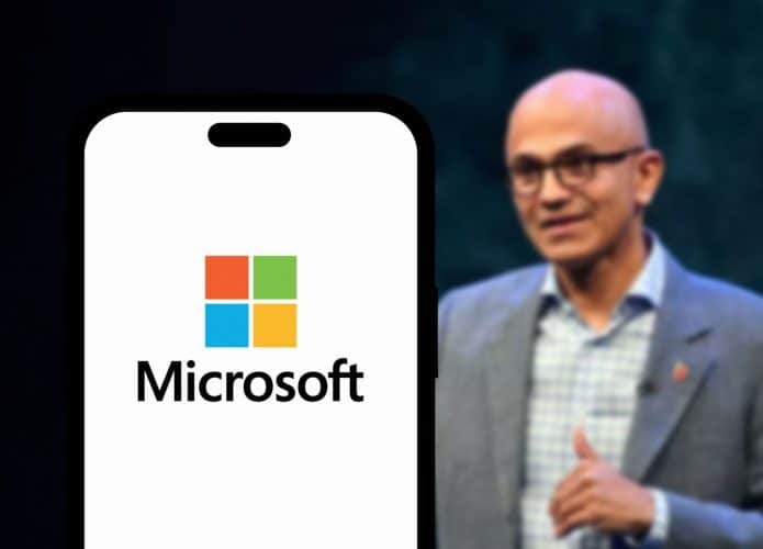 Satya Nadella ao lado de um smartphone exibindo o logo da Microsoft em sua tela