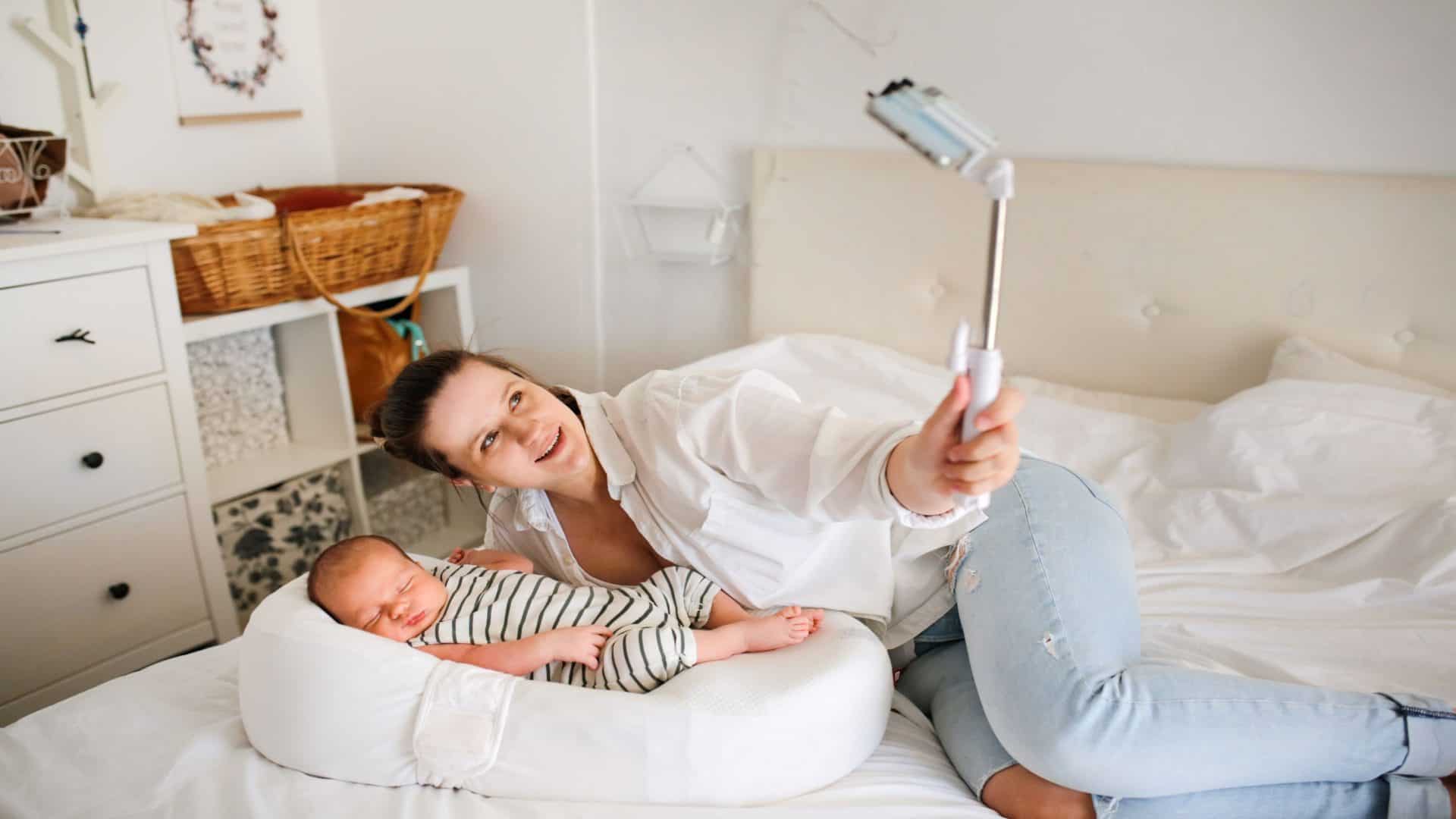 Mãe com um bebê recém-nascido. Mãe usando uma camisa branca tira uma selfie com um pau de selfie em um fundo claro, com uma tonalidade leve. Conceito de redes sociais e comunicação por vídeo