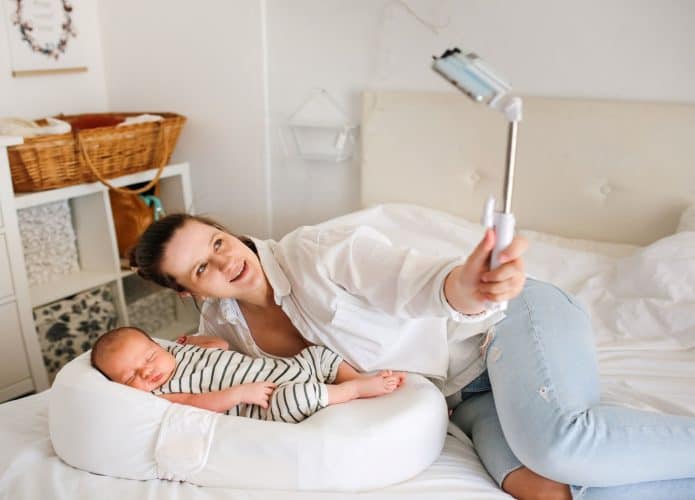 Mãe com um bebê recém-nascido. Mãe usando uma camisa branca tira uma selfie com um pau de selfie em um fundo claro, com uma tonalidade leve. Conceito de redes sociais e comunicação por vídeo