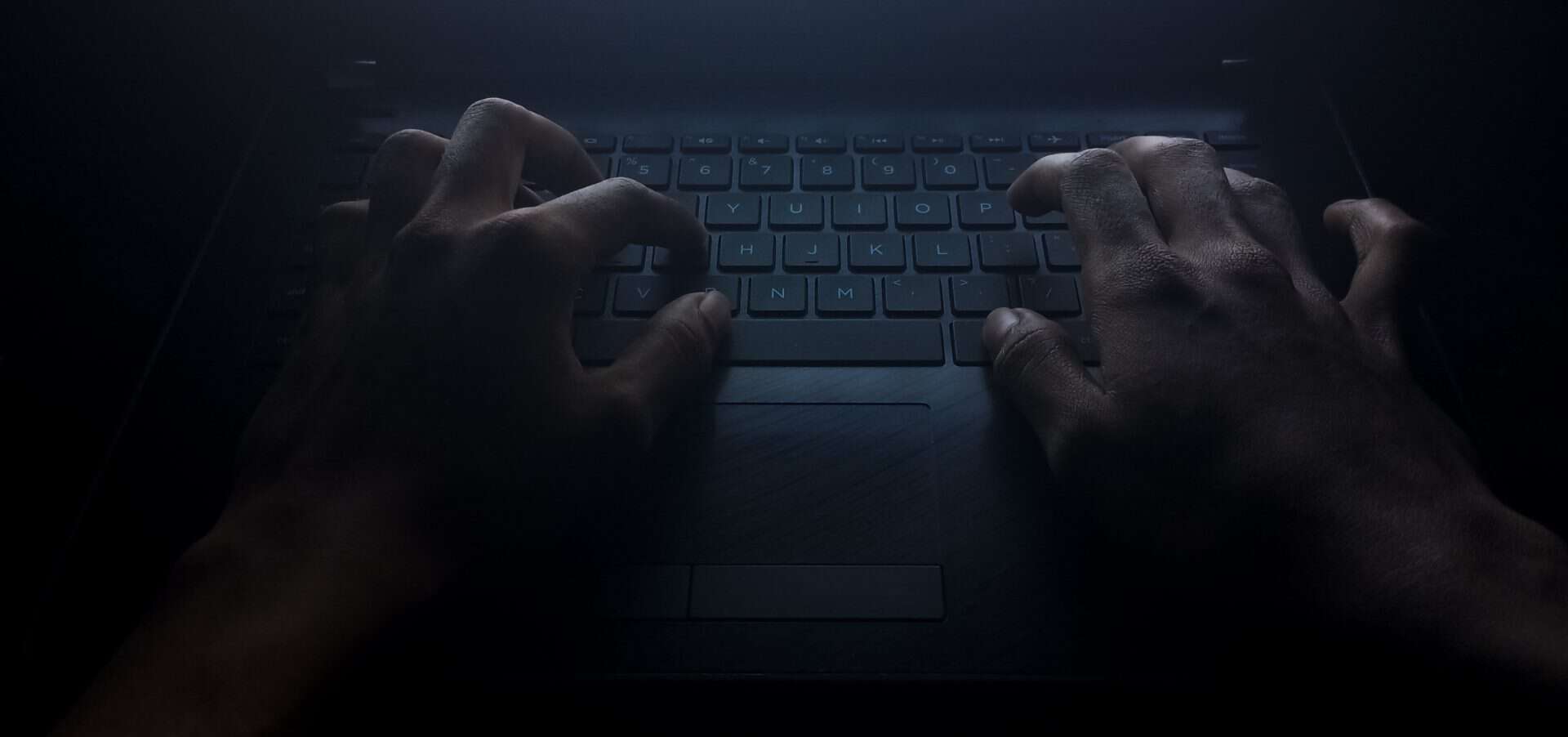 Mão digitando no teclado de um laptop na escuridão