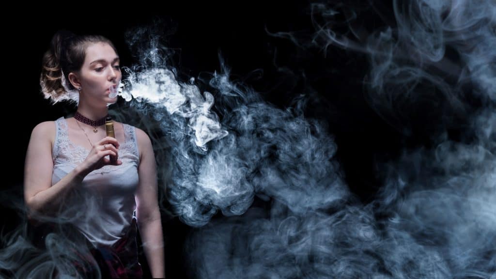 Cigarro eletrônico na mão da vaper. Mulher fuma cigarro de vapor. Vaper está em um lugar escuro.