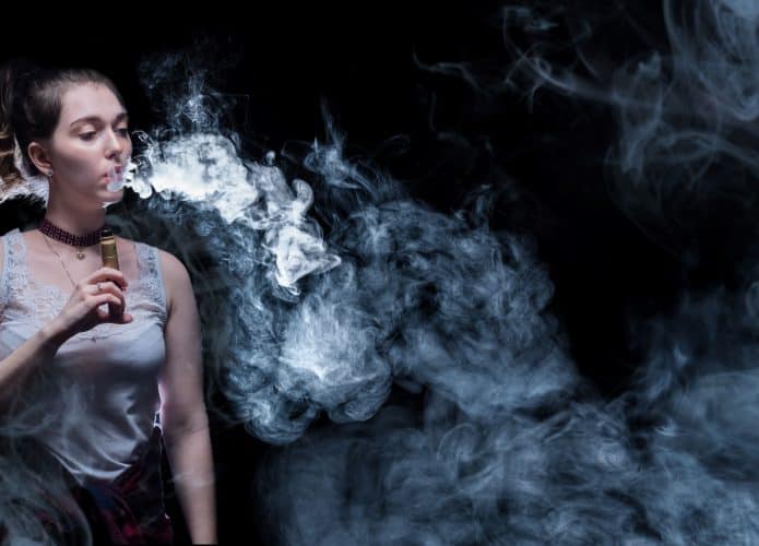 Cigarro eletrônico na mão da vaper. Mulher fuma cigarro de vapor. Vaper está em um lugar escuro.