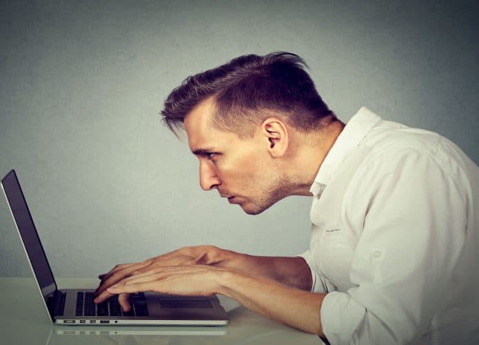 Perfil lateral de um jovem trabalhando no computador, sentado à mesa, isolado no fundo do escritório com parede cinza. Conceito de uma vida longa, monótona e cansativa de horas de trabalho.
