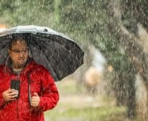 Homem vestindo casaco vermelho segurando guarda-chuva aberto durante chuva na rua