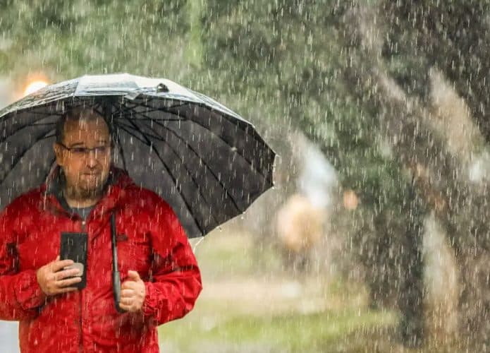 Homem vestindo casaco vermelho segurando guarda-chuva aberto durante chuva na rua