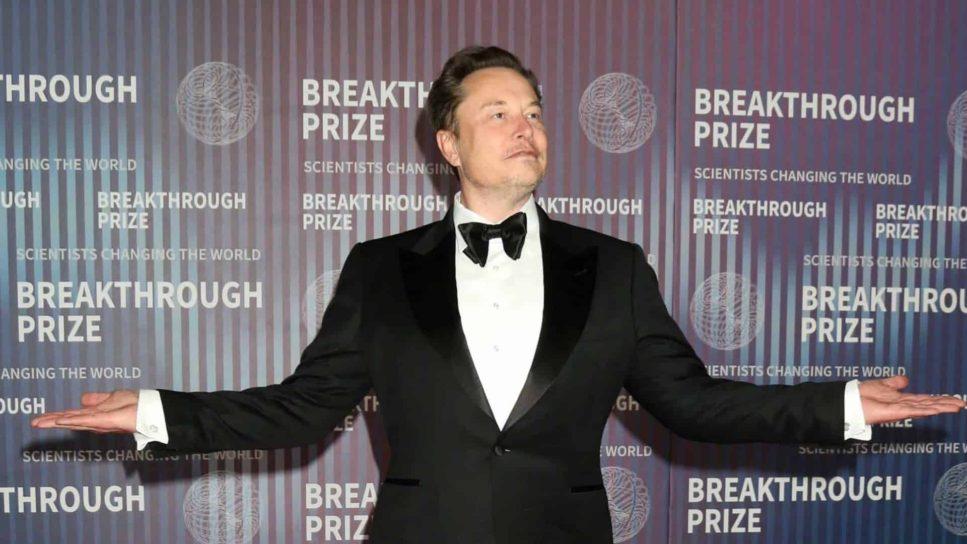 Elon Musk olhado para o lado direito e com os braços abertos