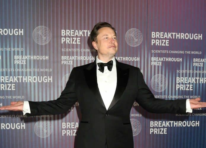 Elon Musk olhado para o lado direito e com os braços abertos