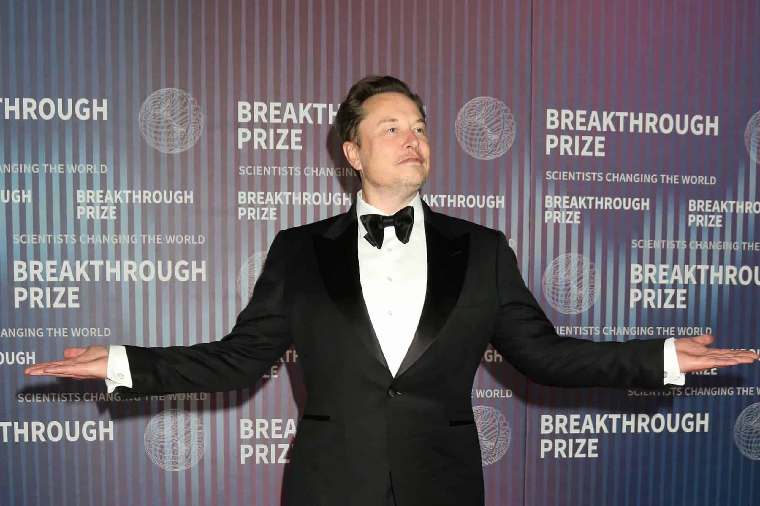 Elon Musk olhado para o lado direito e com os braços abertos