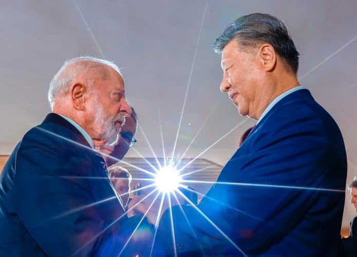 Presidentes da China, Xi Jinping, e do Brasil, Lula, apertando mãos com luz brilhante ao fundo