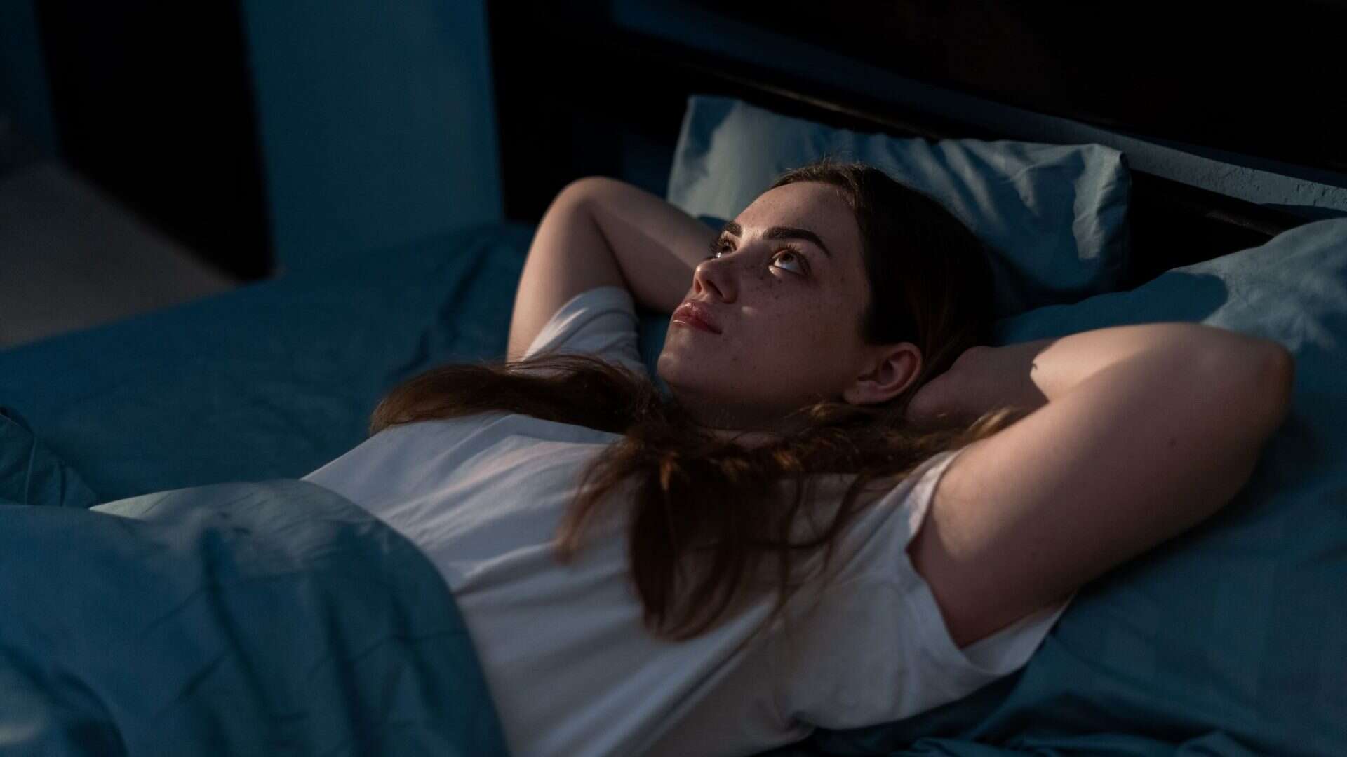Mulher deitada na cama olhando para o teto com os braços cruzados atrás da cabeça