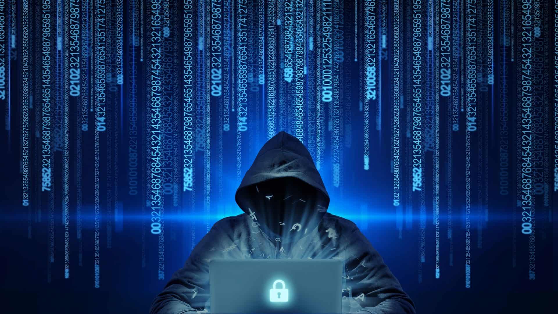 Pessoa com capuz atrás de um notebook