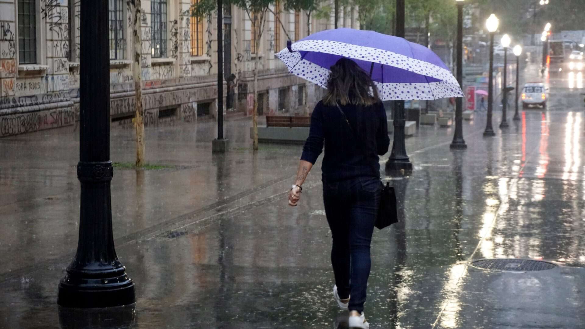 Mulher com guarda-chuva andando em uma rua de São Paulo enquanto chove