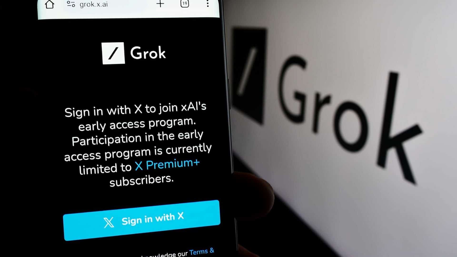 Página do Grok em um smartphone, ao lado do logo do chatbot impresso em uma parede