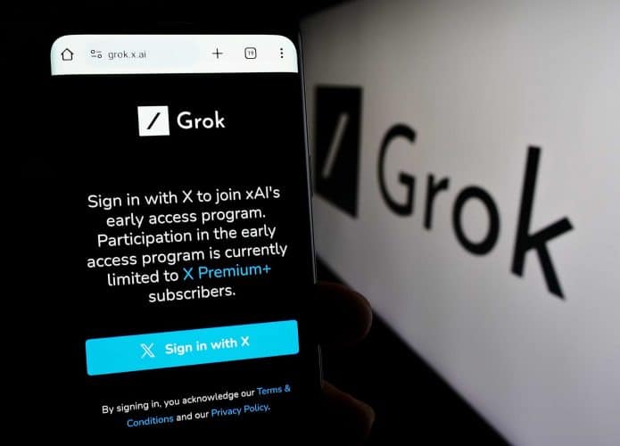 Página do Grok em um smartphone, ao lado do logo do chatbot impresso em uma parede
