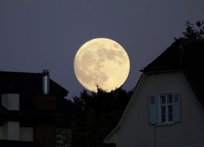 Foto da lua cheia com silhuetas de casas grandes na frente