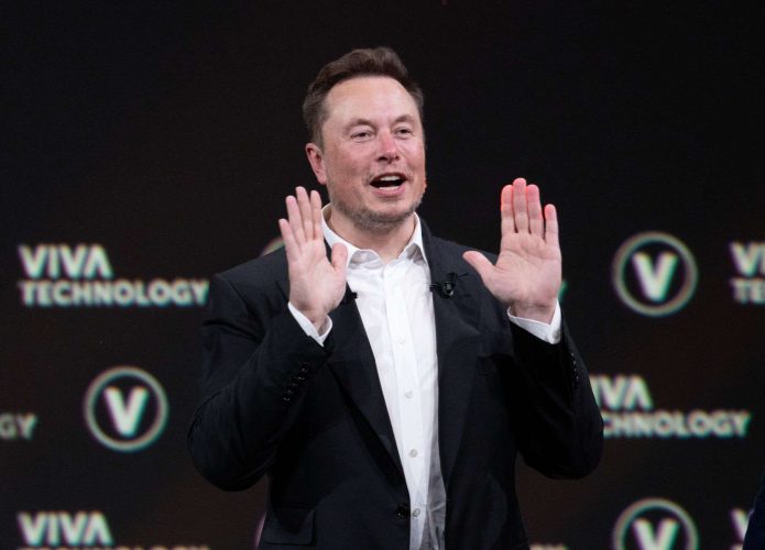 Elon Musk com a boca aberta e as mãos espalmadas