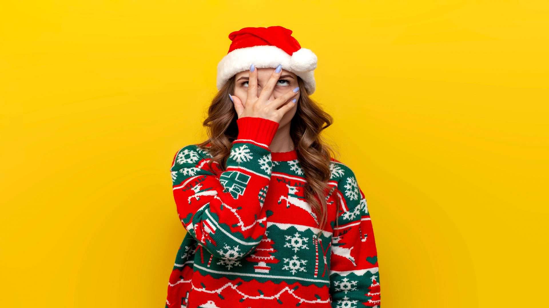 garota confusa em suéter de natal e chapéu do papai noel cobre o rosto com a mão em fundo amarelo isolado, mulher