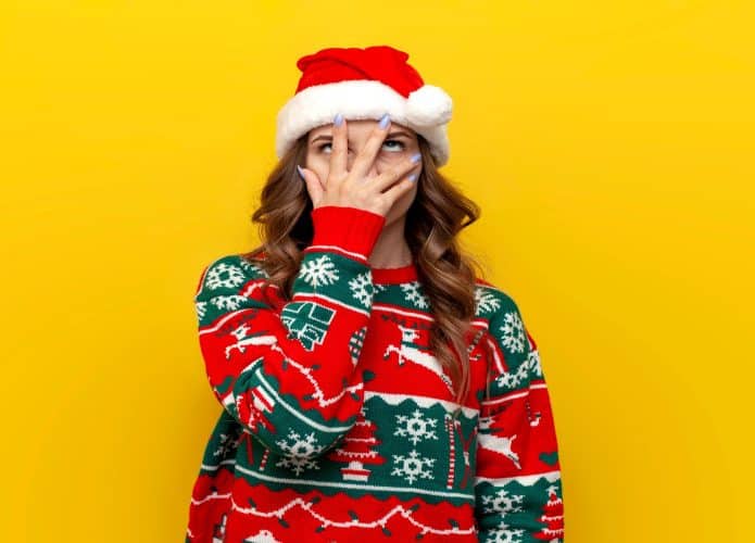 garota confusa em suéter de natal e chapéu do papai noel cobre o rosto com a mão em fundo amarelo isolado, mulher