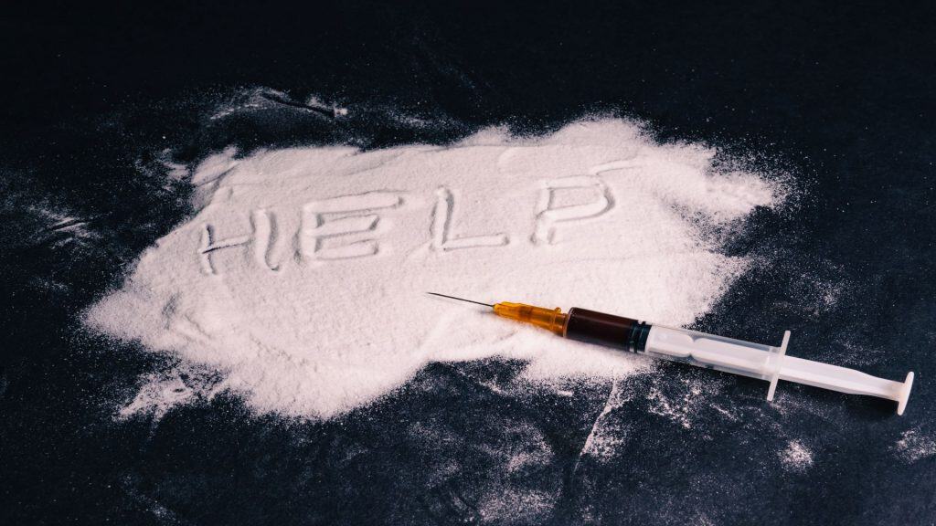 Conceito de dependência química. Heroína é derramada sobre a mesa, a palavra ajuda está escrita nela e há uma seringa com uma dose sobre ela. Fundo preto. Fundo preto. Foto de alta qualidade.