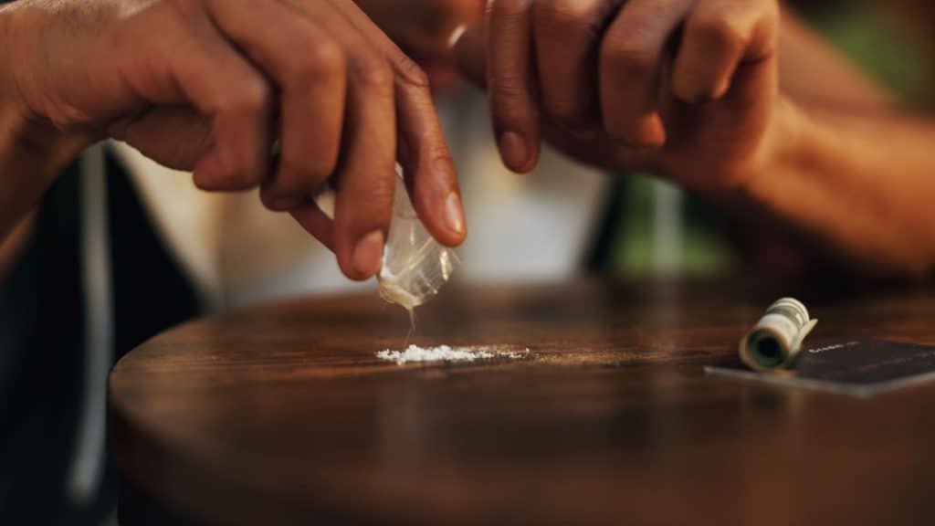 Pessoa, casa e mão com cocaína, drogas e substância ilegal com vício. Overdose, evento e noite com closeup, hábito ou baixa energia com crime, reabilitação ou cartão de crédito na sala de estar