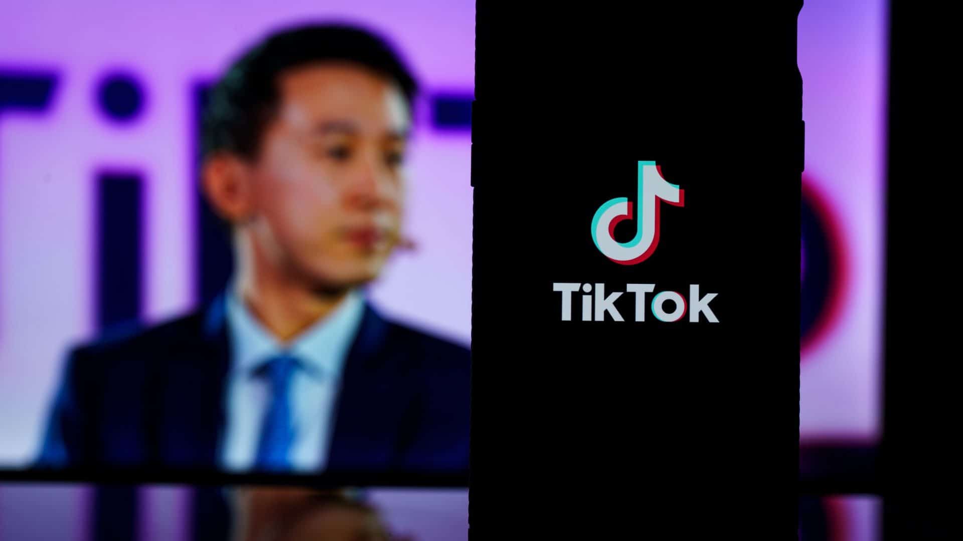 Celular com logotipo do TikTok na tela na frente de monitor com foto do CEO do TikTok, Shou Zi Chew