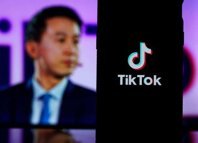 Celular com logotipo do TikTok na tela na frente de monitor com foto do CEO do TikTok, Shou Zi Chew
