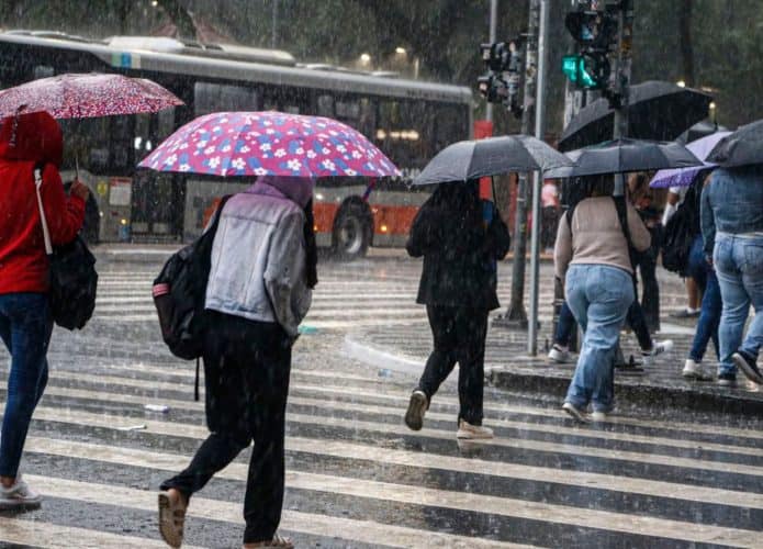 Pessoas atravessando avenida segurando guarda-chuva em dia chuvoso