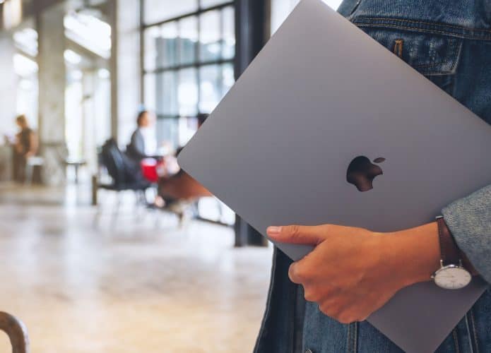 Pessoa segurando MacBook em lugar público