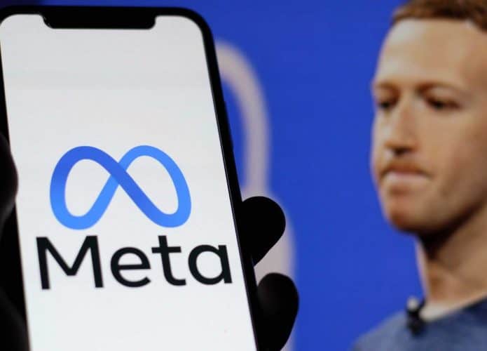 Celular com logomarca da Meta na tela na frente de monitor com foto de Mark Zuckerberg com cara franzida