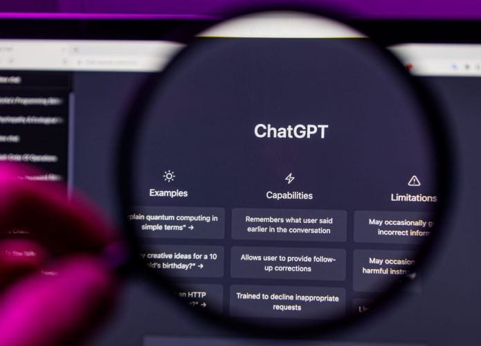 Foto estilo POV de pessoa segurando lupa sobre tela de notebook com ChatGPT aberto