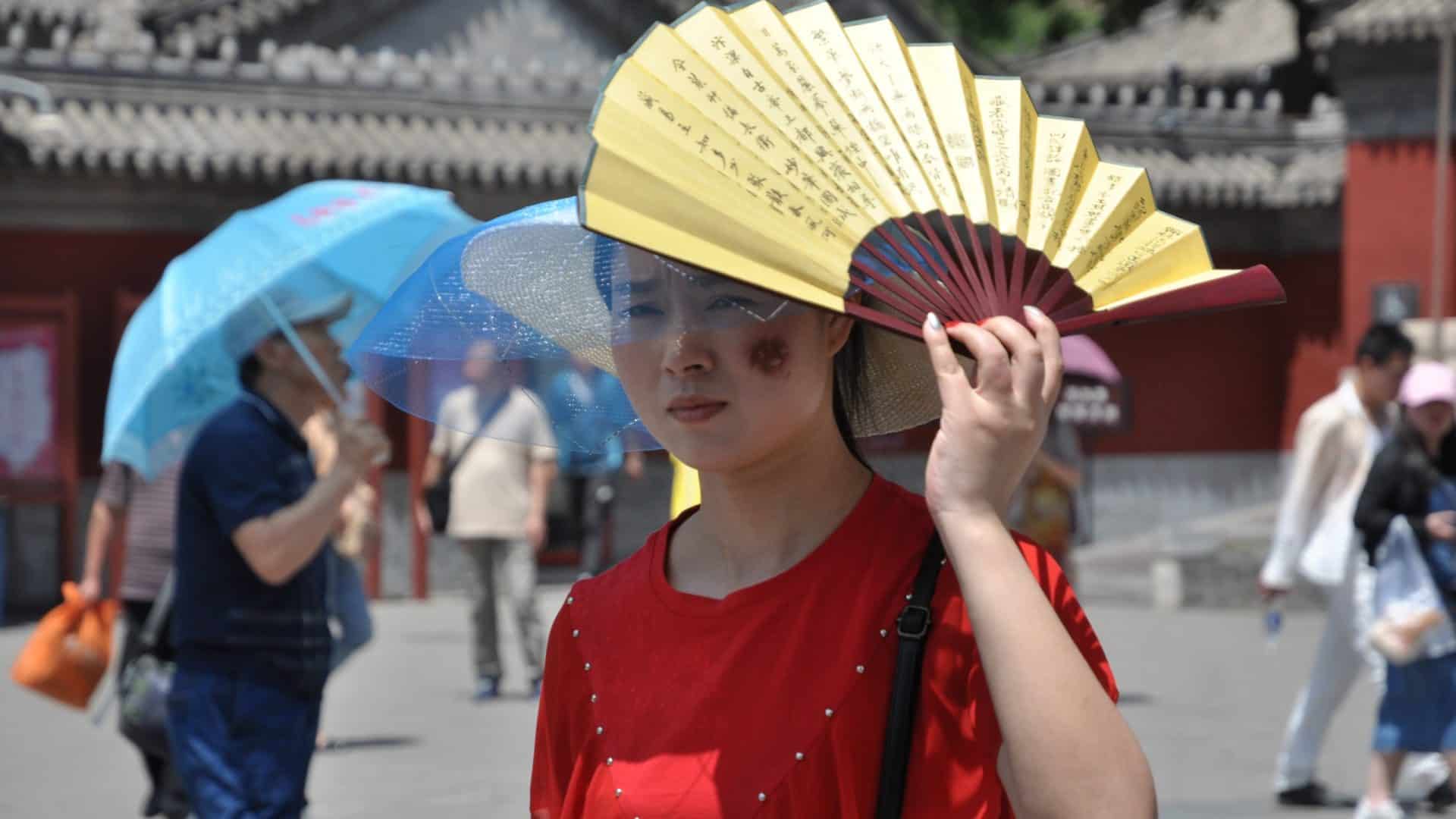 Mulher colocando o leque sobre a cabeça em dia de Sol