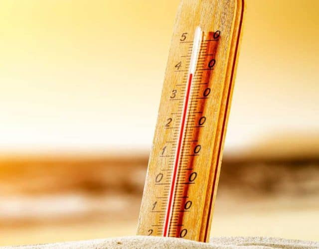 Termômetro de mercúrio fincado em areia de deserto em dia quente