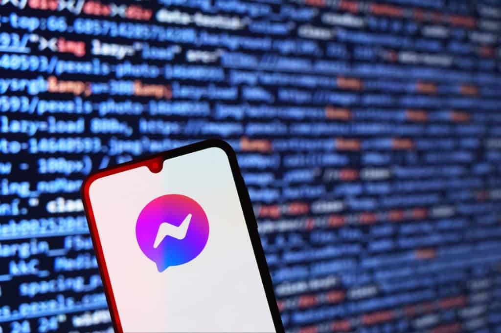 Logo do Messenger em um smartphone; atrás, linhas de códigos de computador