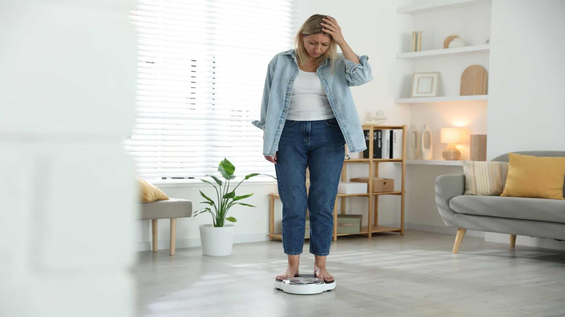 Menopausa, ganho de peso. Mulher preocupada em pé em escalas de chão em casa