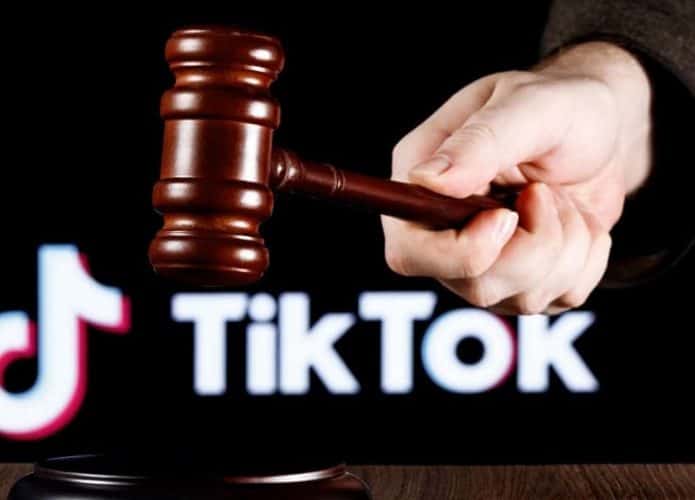 À frente, um martelo de juiz segurado por uma mão; abaixo, uma mesa; atrás, desfocado, o logotipo do TikTok