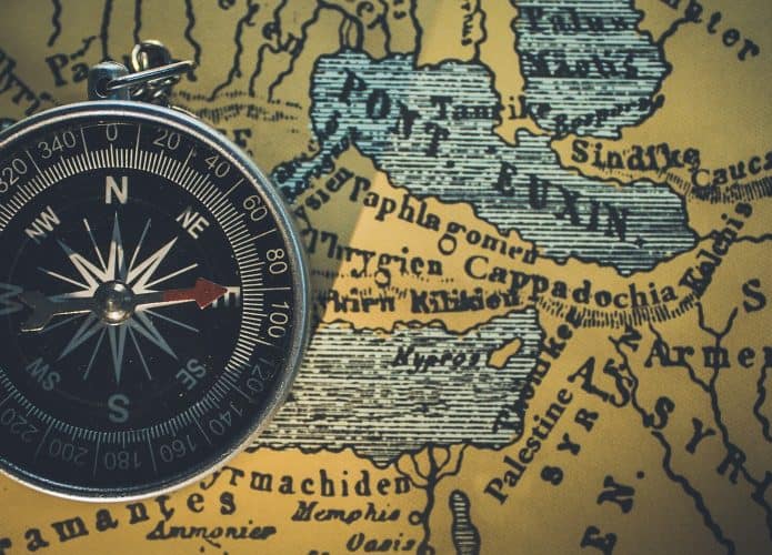 Uma bússola metálica em close-up, com ponteiros apontando para o norte e o sul, colocada sobre um mapa histórico que destaca regiões antigas como Armênia e Síria. Crédito: Himesh Kumar Behera, thehopefultraveller, CC0, via Wikimedia Commons.
