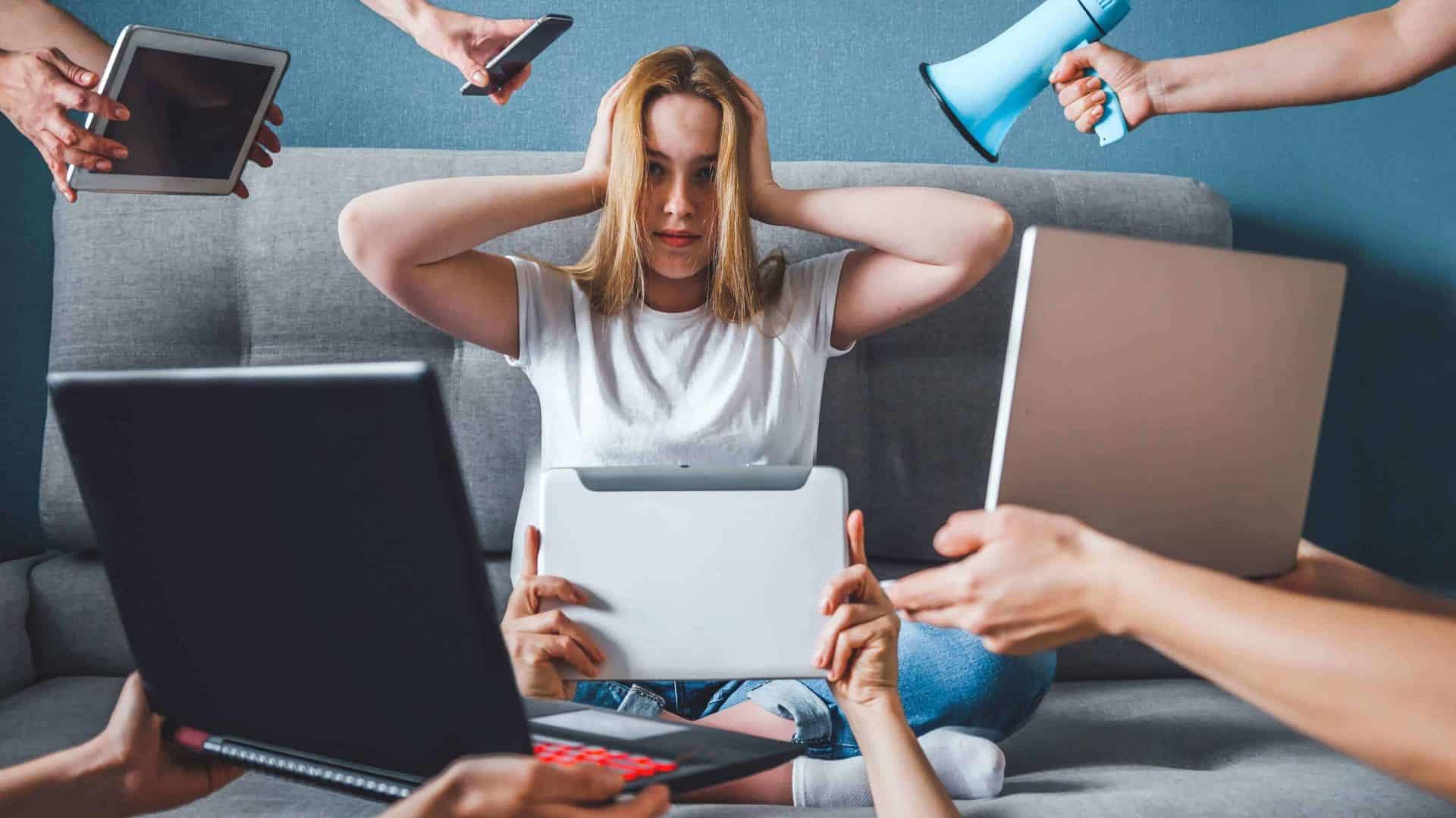 Mulher com as mãos na cabeça, rodeada por dispositivos eletrônicos