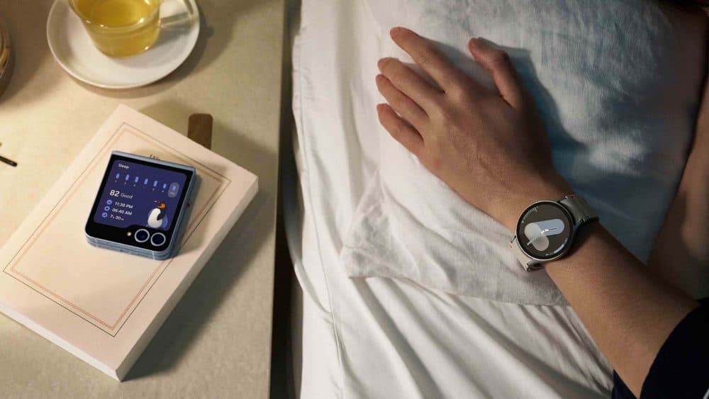 braço com um Galaxy Watch no pulso sobre uma cama ao lado de uma mesa de cabeceira