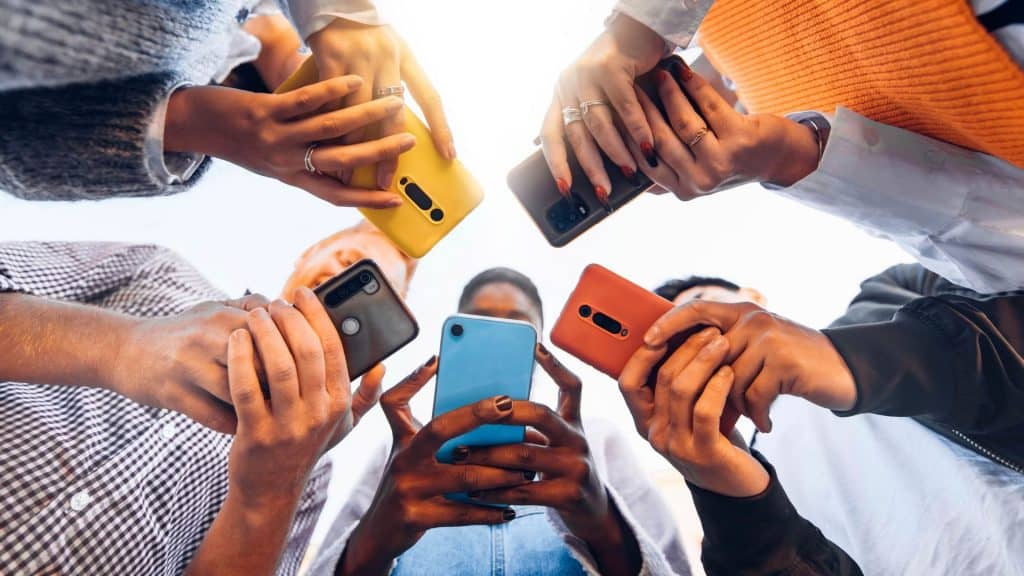 Na imagem, jovens utilizam seus celulares