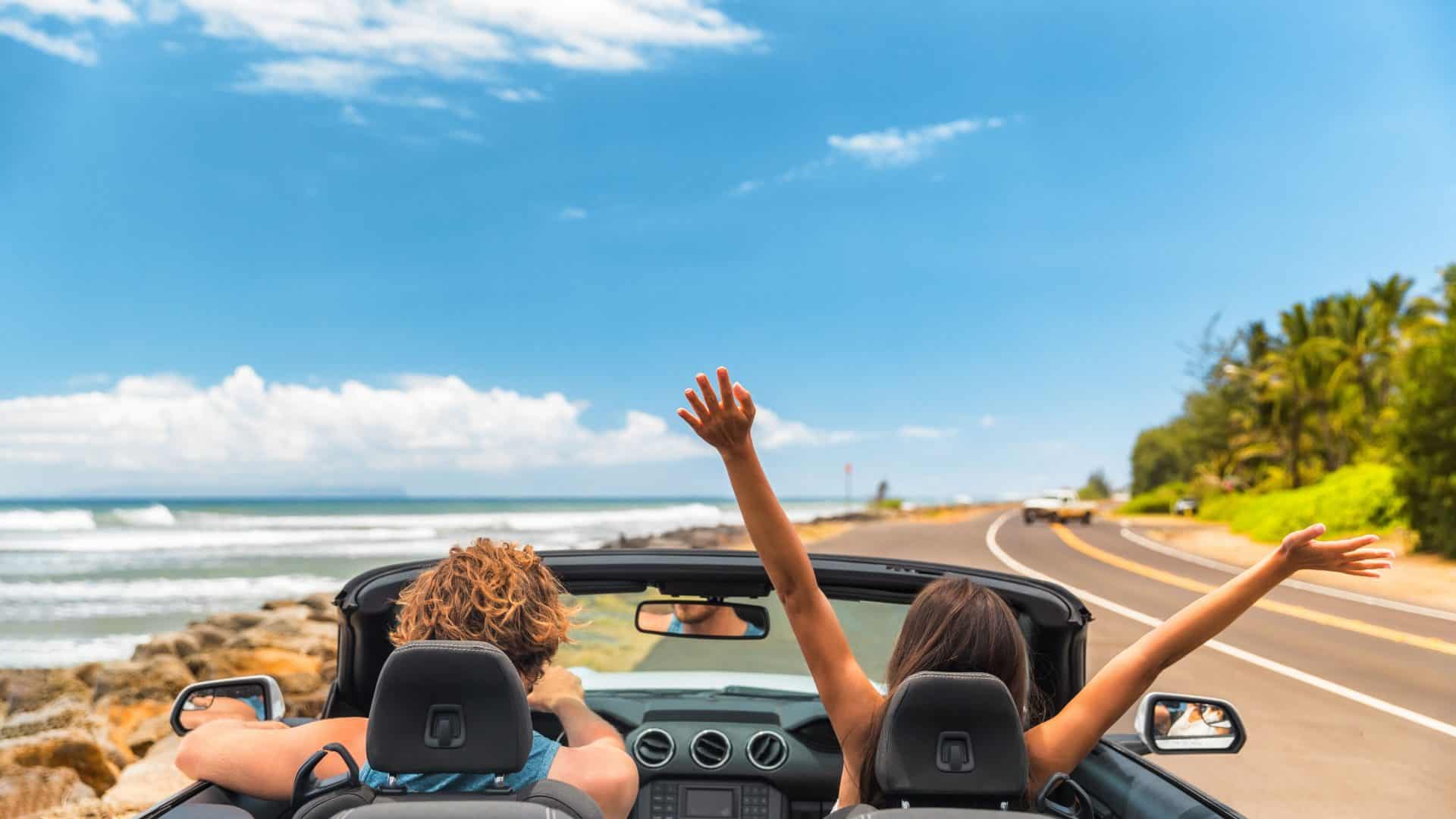 Viagem de carro férias felizes casal dirigindo um carro conversível nas férias de verão no Havai. Mulher com os braços para cima se divertindo, jovem homem ao volante.