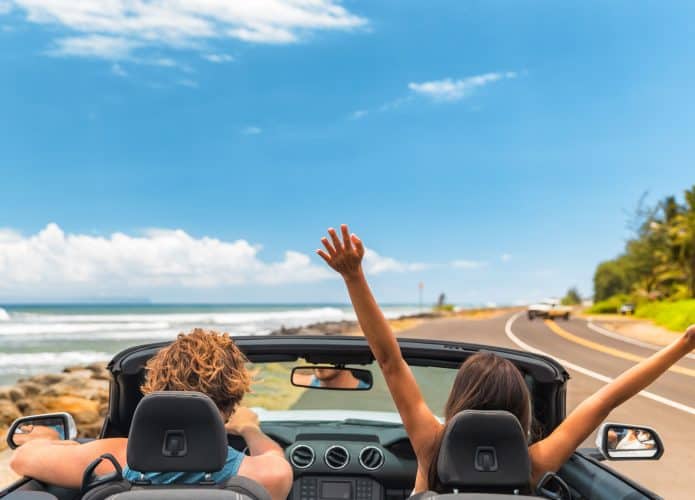 Viagem de carro férias felizes casal dirigindo um carro conversível nas férias de verão no Havai. Mulher com os braços para cima se divertindo, jovem homem ao volante.