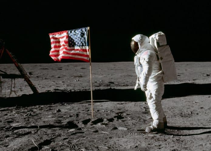 Bandeira dos Estados Unidos tremulando na superfície Lua enquanto astronauta está de pé ao lado dela