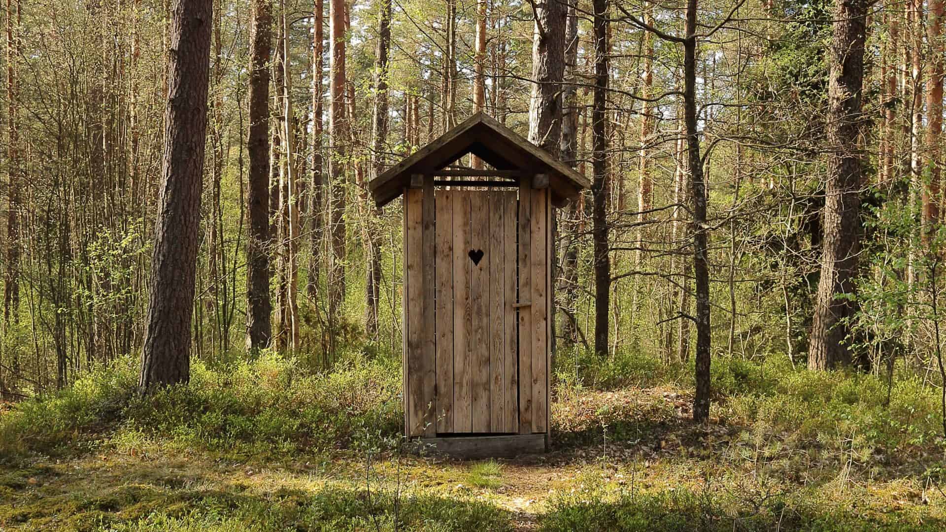 Cabine antiga de banheiro feita de madeira e vista de longe numa floresta