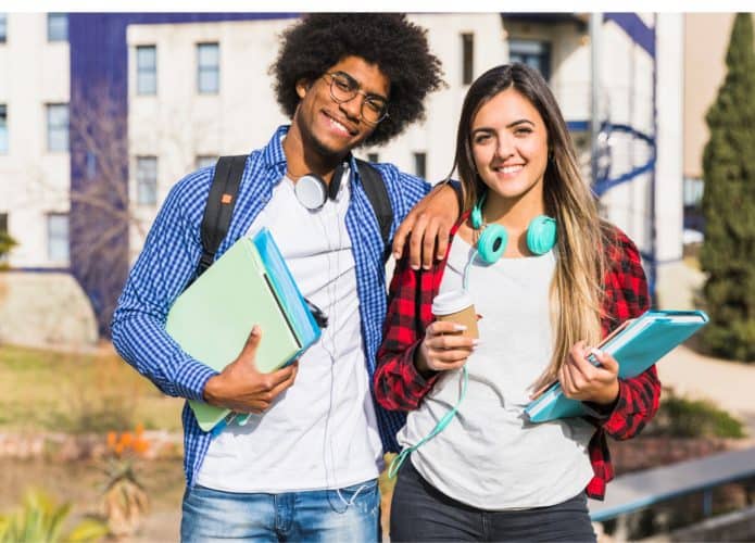 Um casal de estudantes lado a lado, segurando cadernos e com fones de ouvido