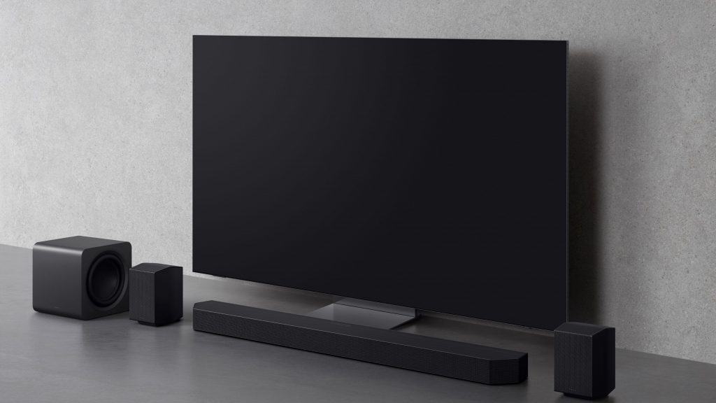Modelo de soundbar da Samsung HW-Q990F instalado em TV da marca colocada sobre chão numa casa minimalista