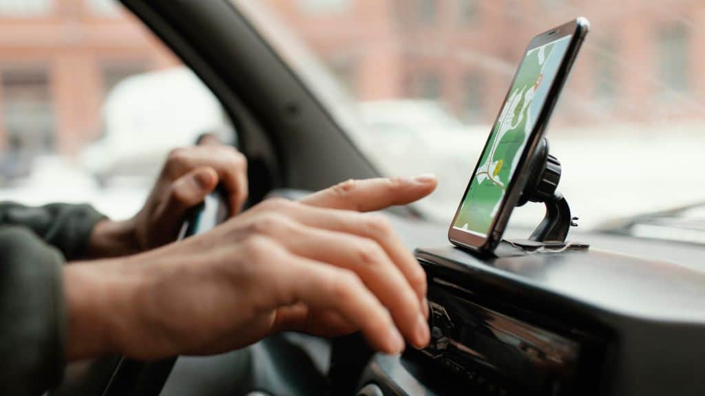 Mãos no volante e no celular, interagindo com um app de transporte enquanto o carro está estacionado, refletindo o uso prático do aplicativo