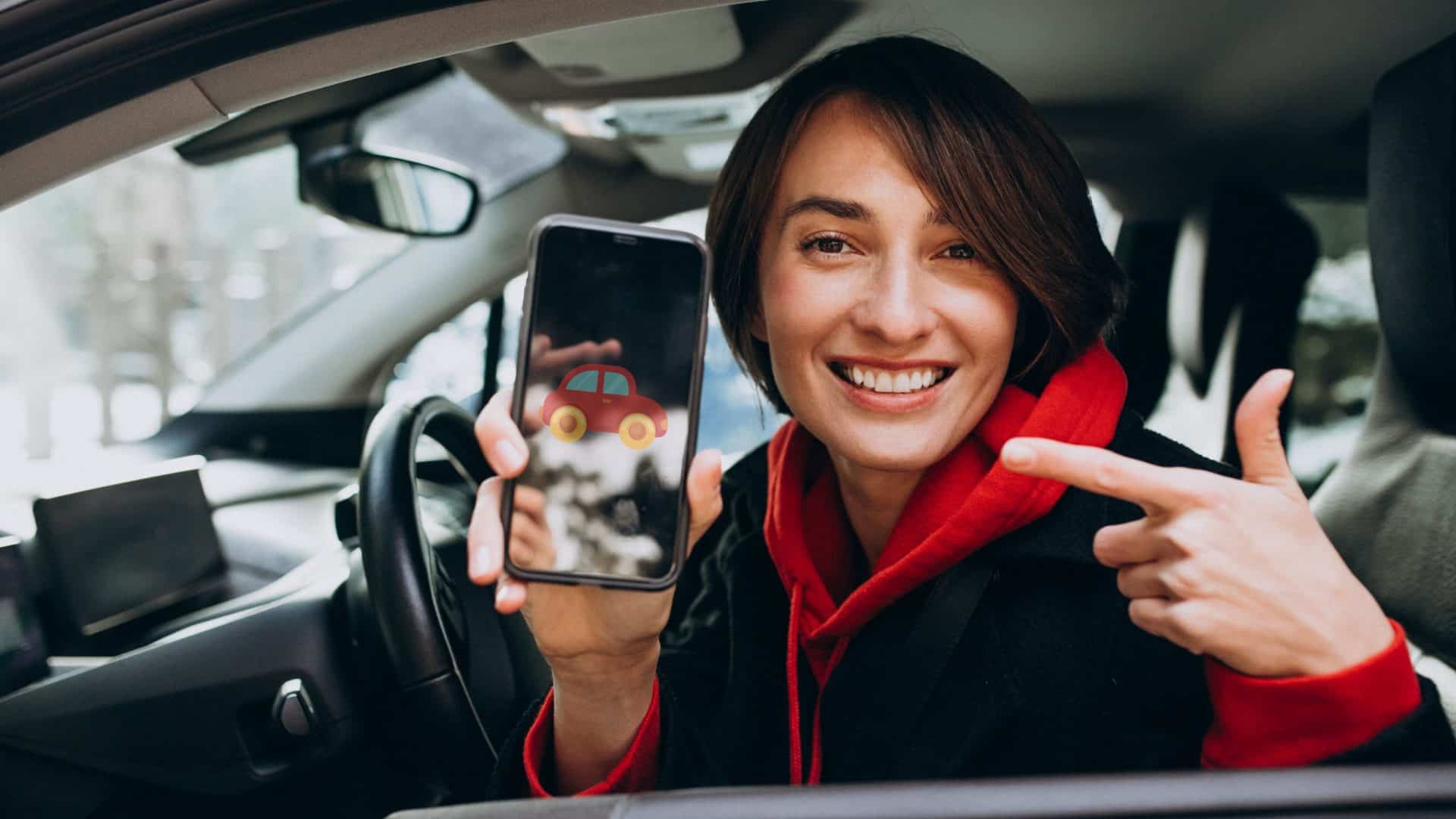 Mulher dentro de um carro, no banco do motorista, sorrindo e segurando o celular com um ícone de carro na tela, representando o uso de apps de transporte