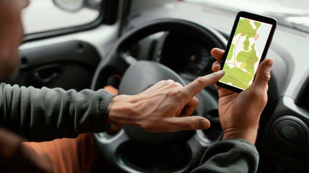 Uma combinação das cenas anteriores, com as mãos no volante e no celular, interagindo com o app de transporte enquanto o carro está no trânsito.